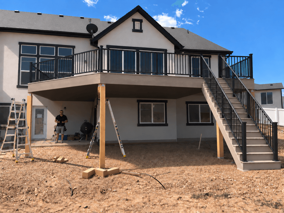 Raised deck with wrought iron railing and an open stair down to grade on a new-build home, still under construction.