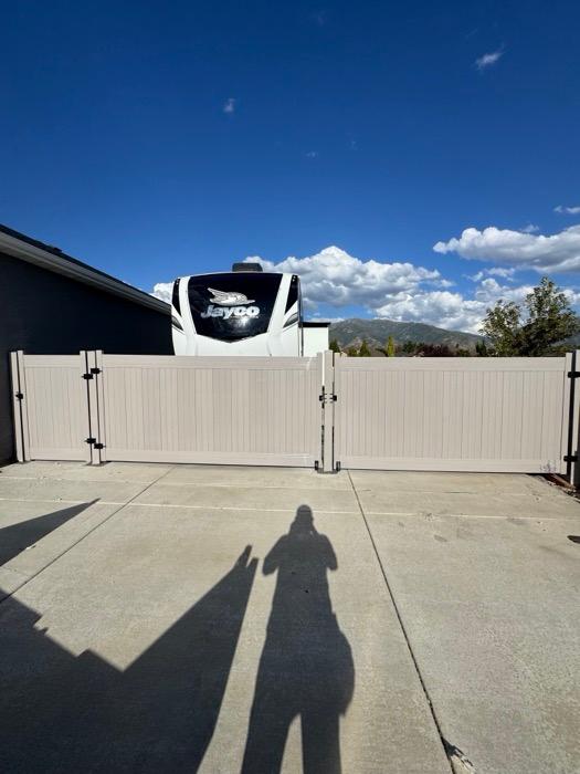 Tan vinyl RV gates across a concrete driveway, with a narrower personal gate alongside.