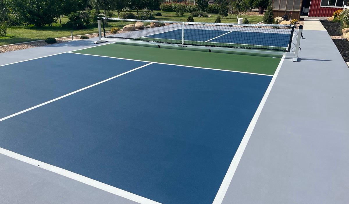 Navy and grass green pickleball court in Mapleton with an orchard and red barn behind