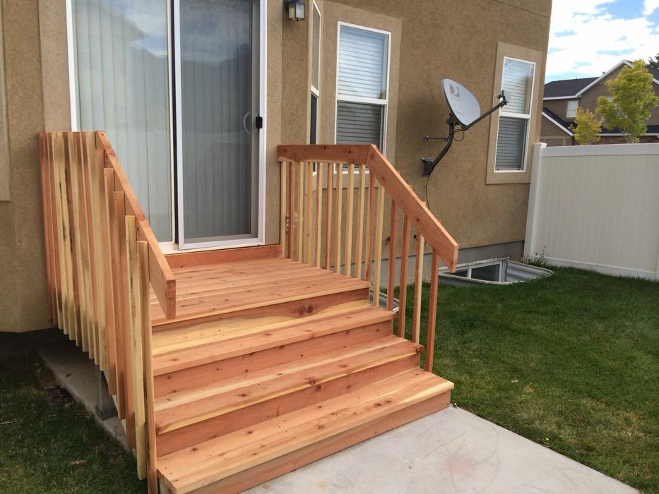 Timber exterior staircase in Spanish Fork running from a sliding door down to a concrete walk, with matching handrails both sides.