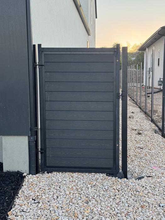 Composite fence and gate in Herriman, dark horizontal slats in a matching frame on black metal posts in a side yard.