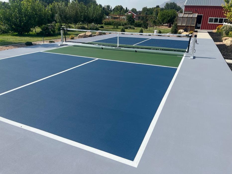 Mapleton pickleball court from the baseline, net in place and the light grey apron running out to the edge of the slab.