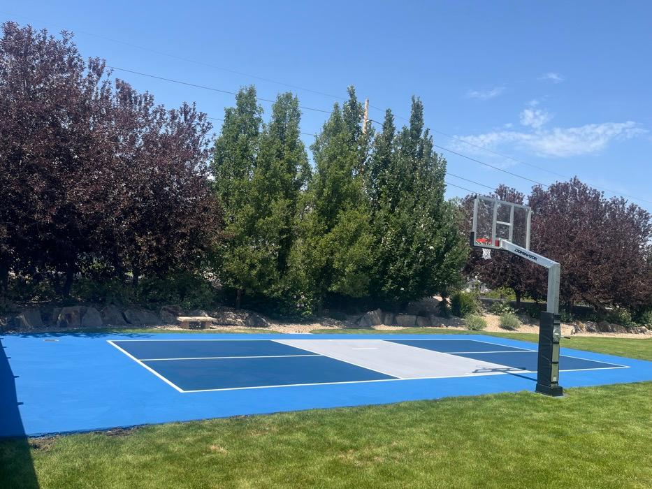 Bountiful multi-sport court with a Dominator glass-backboard hoop on a padded base pole at the end of the pickleball court.