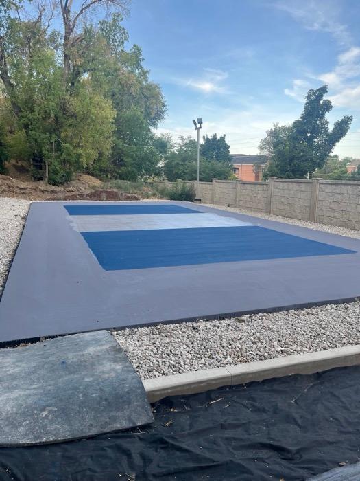 Pickleball court in Orem part-built, navy surface and grey surround before the lines and second coat go on, precast wall behind.