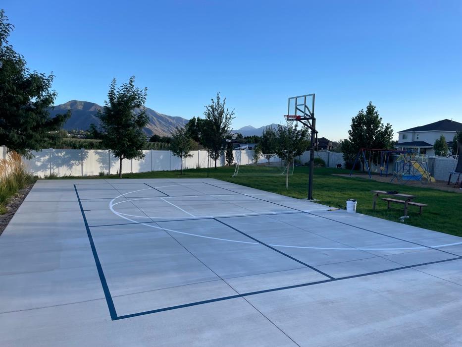 Basketball court in Springville painted straight onto broom-finished concrete, blue and white lines over bare grey with no base coat.