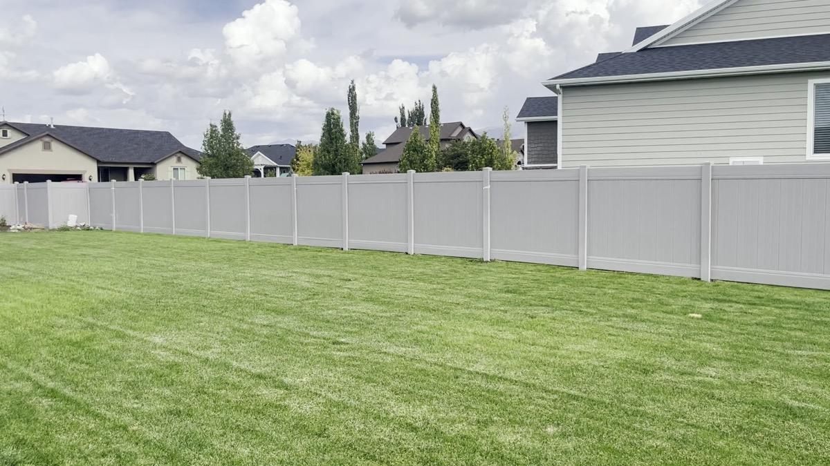 White vinyl privacy fence running the full length of a back lawn in west Kaysville, panels between capped posts, neighbouring houses beyond.