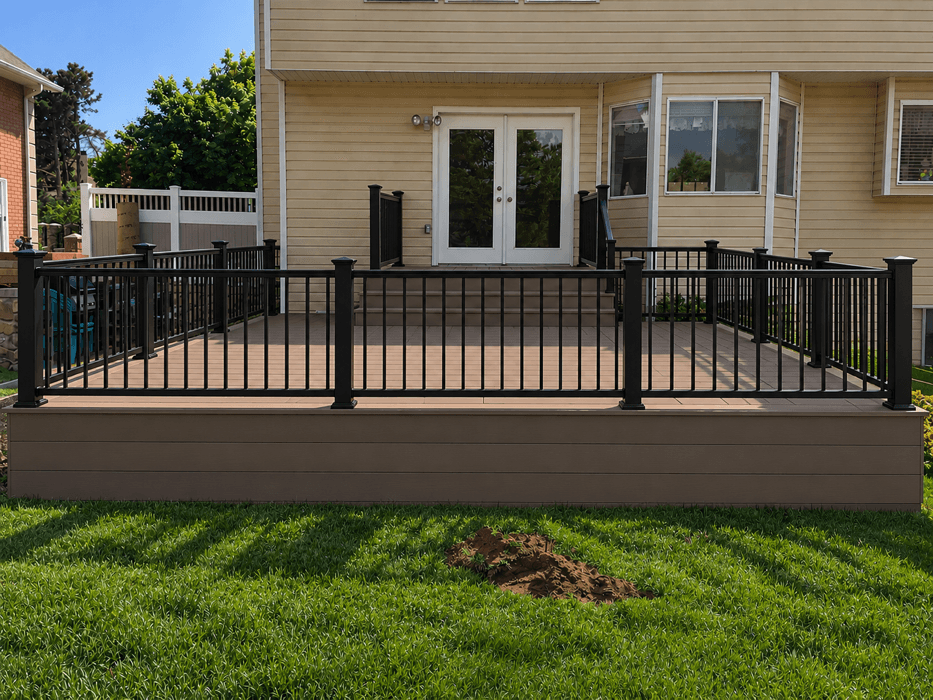 Composite deck in Bountiful with black metal railing and post caps, fascia skirting the full run, against a cream-sided house with French doors.