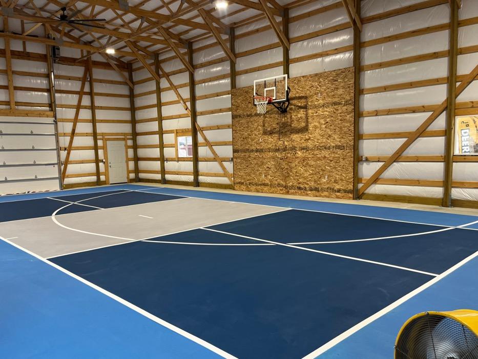 Indoor pickleball and basketball court in a Lehi shop building, sky blue surround with navy zones and a wall-mounted hoop.
